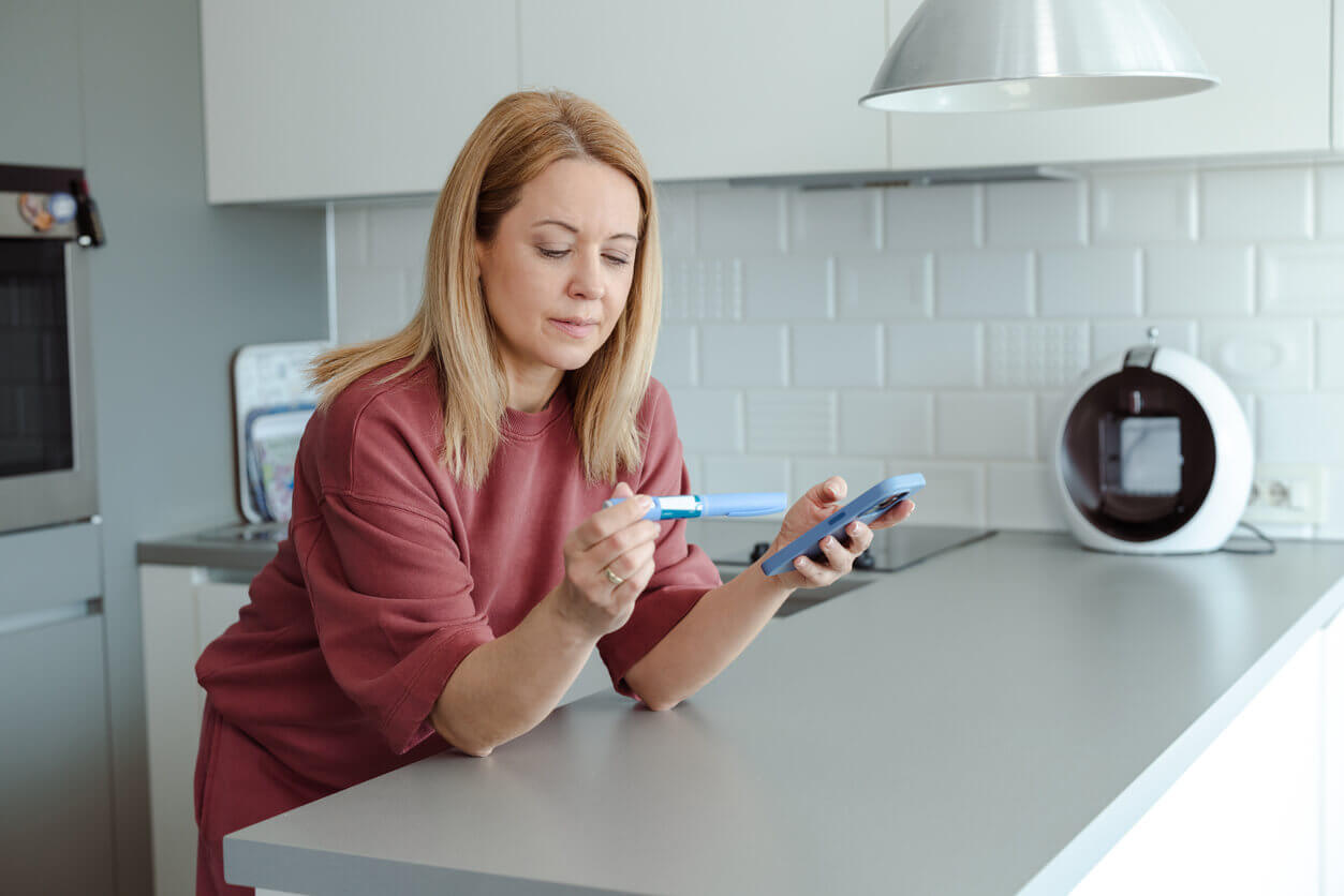 A woman who wants to lose weight is using a smartphone while holding a weight loss injection similar to Wegovy.